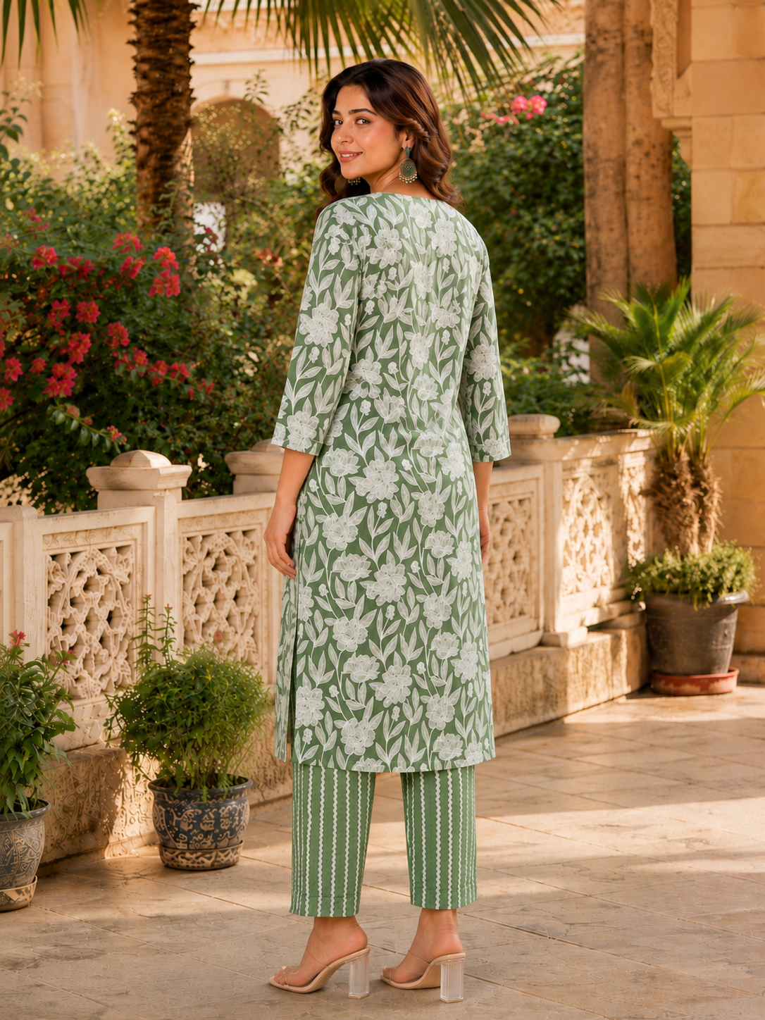 A woman modeling a light green and white printed kurta with matching striped pants, standing in an outdoor courtyard setting.