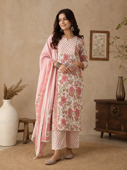 A woman models a traditional Indian kurta with pant and dupatta suit set in a warm, neutral-toned room. The set features a light pink and white floral printed kurta with matching pants and a coordinating dupatta.